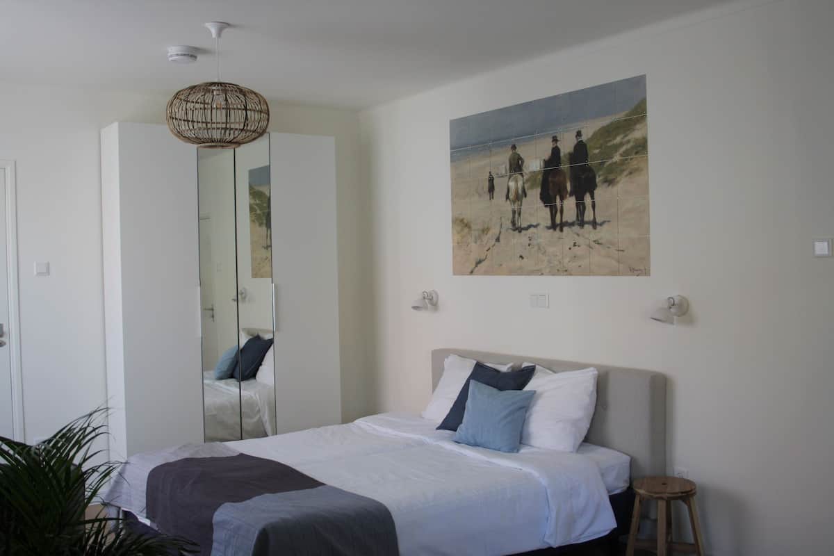 Un dormitorio con cama, espejo, cuadro y lámpara colgante.