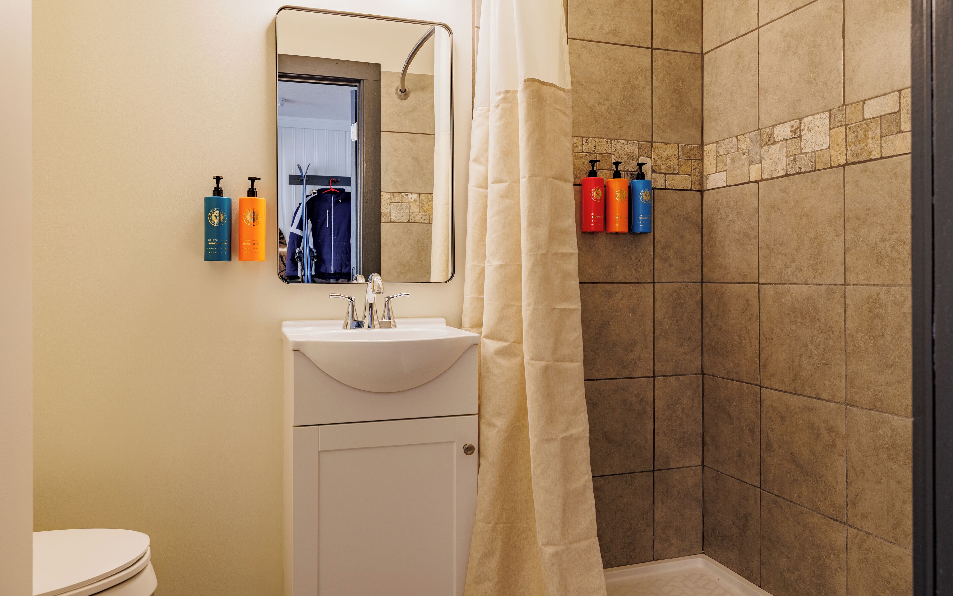 Ein Badezimmer mit Waschbecken, Spiegel, Duschvorhang und Pflegeprodukten an der Wand.