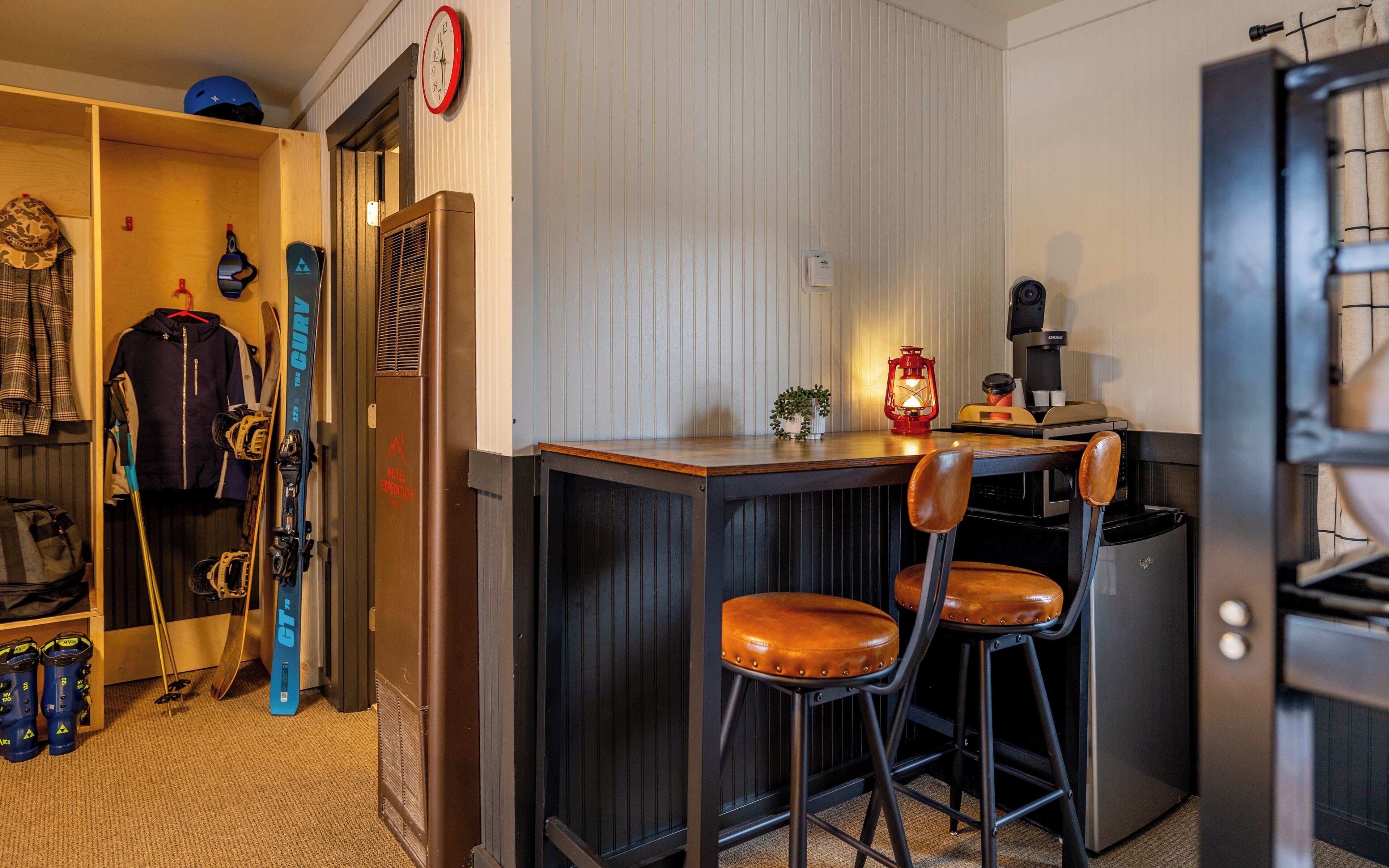 A compact kitchen with a wooden countertop, two stools, a coffee machine, and a red lantern.