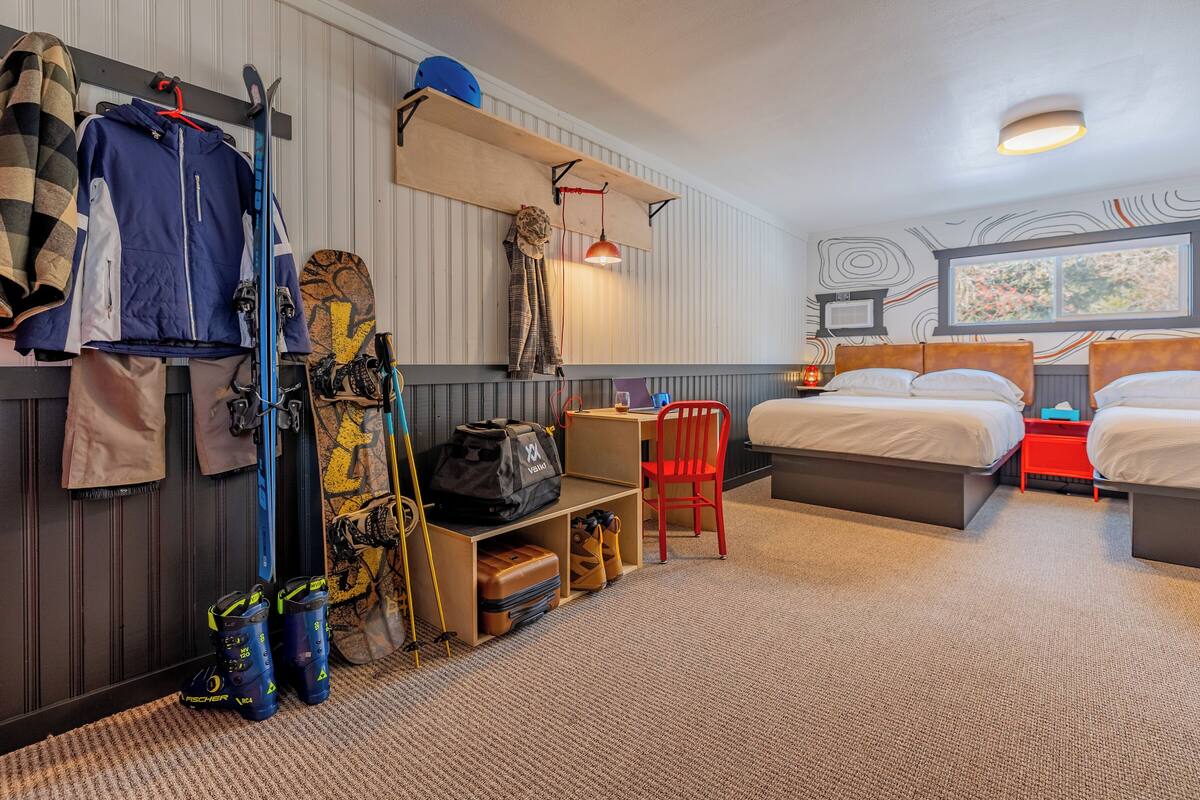 Ein Hotelzimmer mit Bett, Schreibtisch, einem Laptop, einem Stuhl, Skiern und Skiausrüstung.