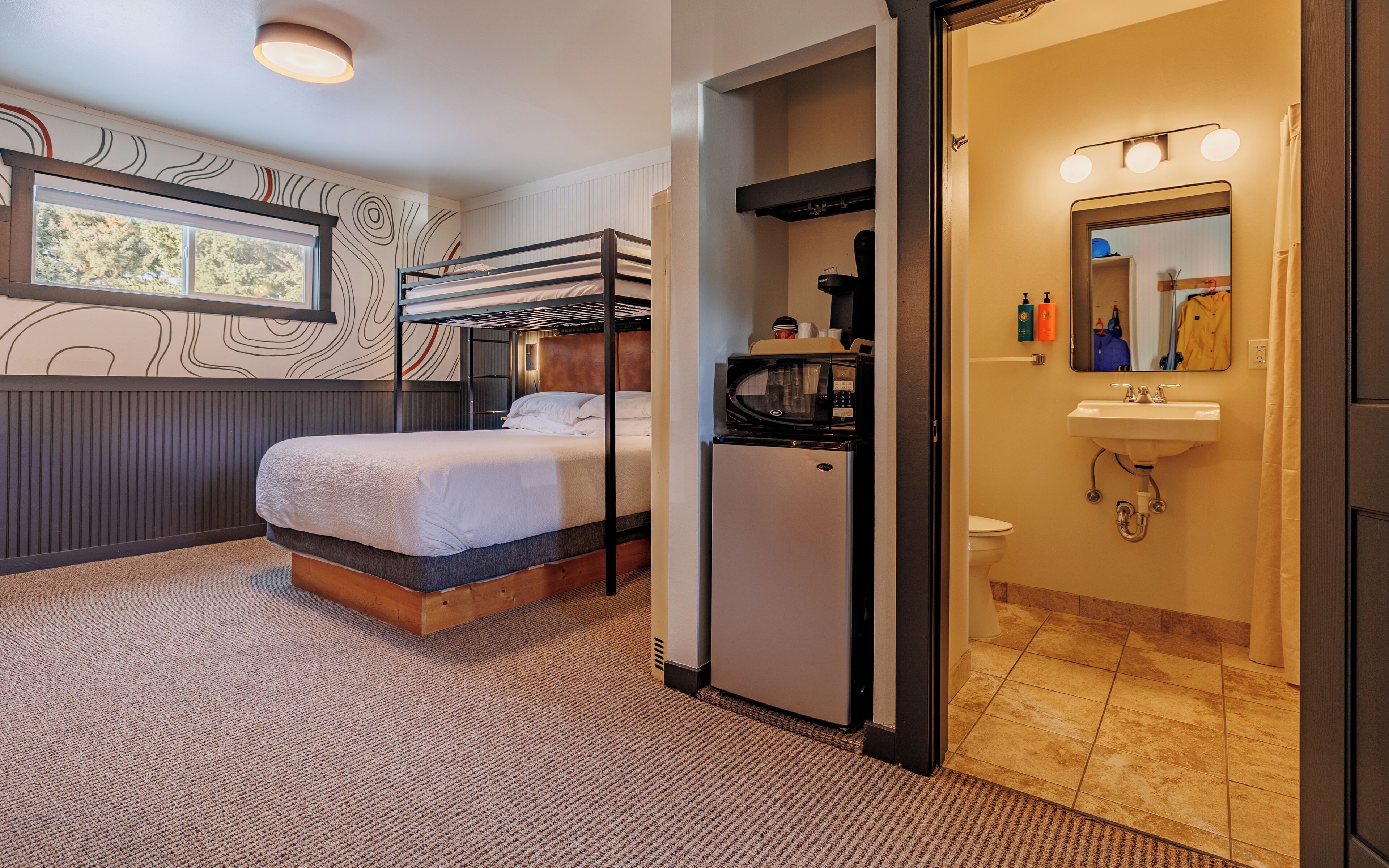 A compact hotel room with a bunk bed, a refrigerator, a microwave, a sink, and a mirror in the bathroom.