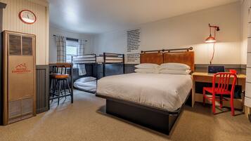 A hotel room with bunk beds, a desk with a chair, a red chair, a lamp, a clock, and a radiator.