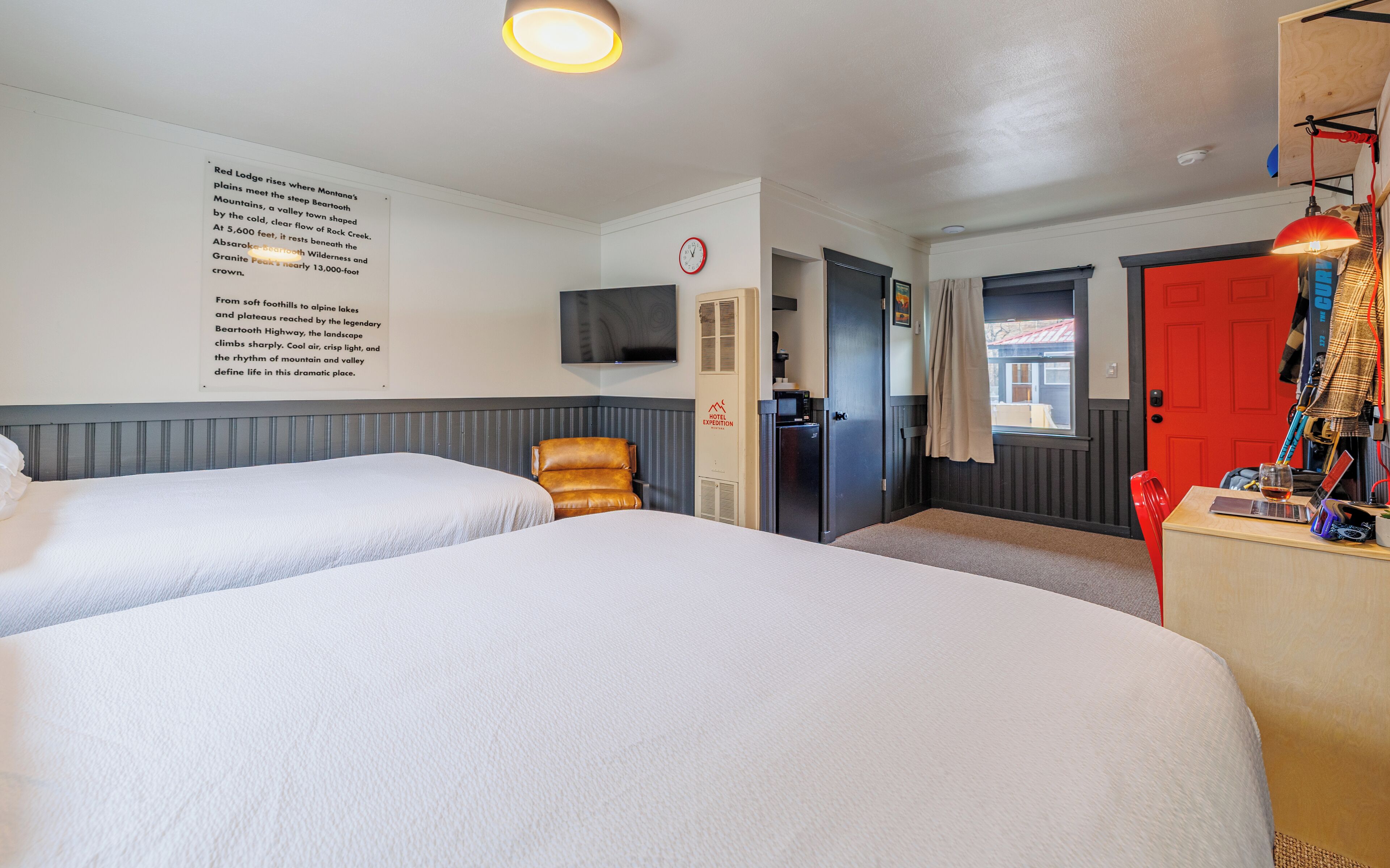 A hotel room with two beds, a TV, a minibar, and a red door.
