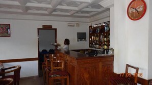 A bar area with wooden furniture, a Coca-Cola clock, and a liquor shelf. - Hotel Altitel (Bafoussam)