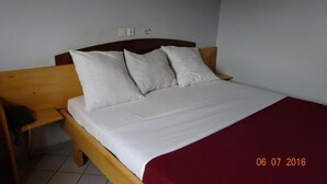 A single bed with a wooden headboard, white bedding, and a red blanket. There is a wooden nightstand to the left of the bed. - Hotel Altitel (Bafoussam)