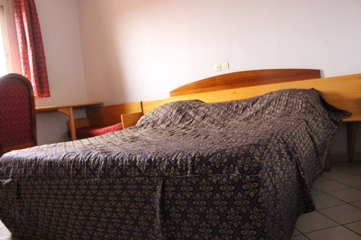 Une pièce comprenant un lit, une tête de lit en bois, une petite table et une chaise.