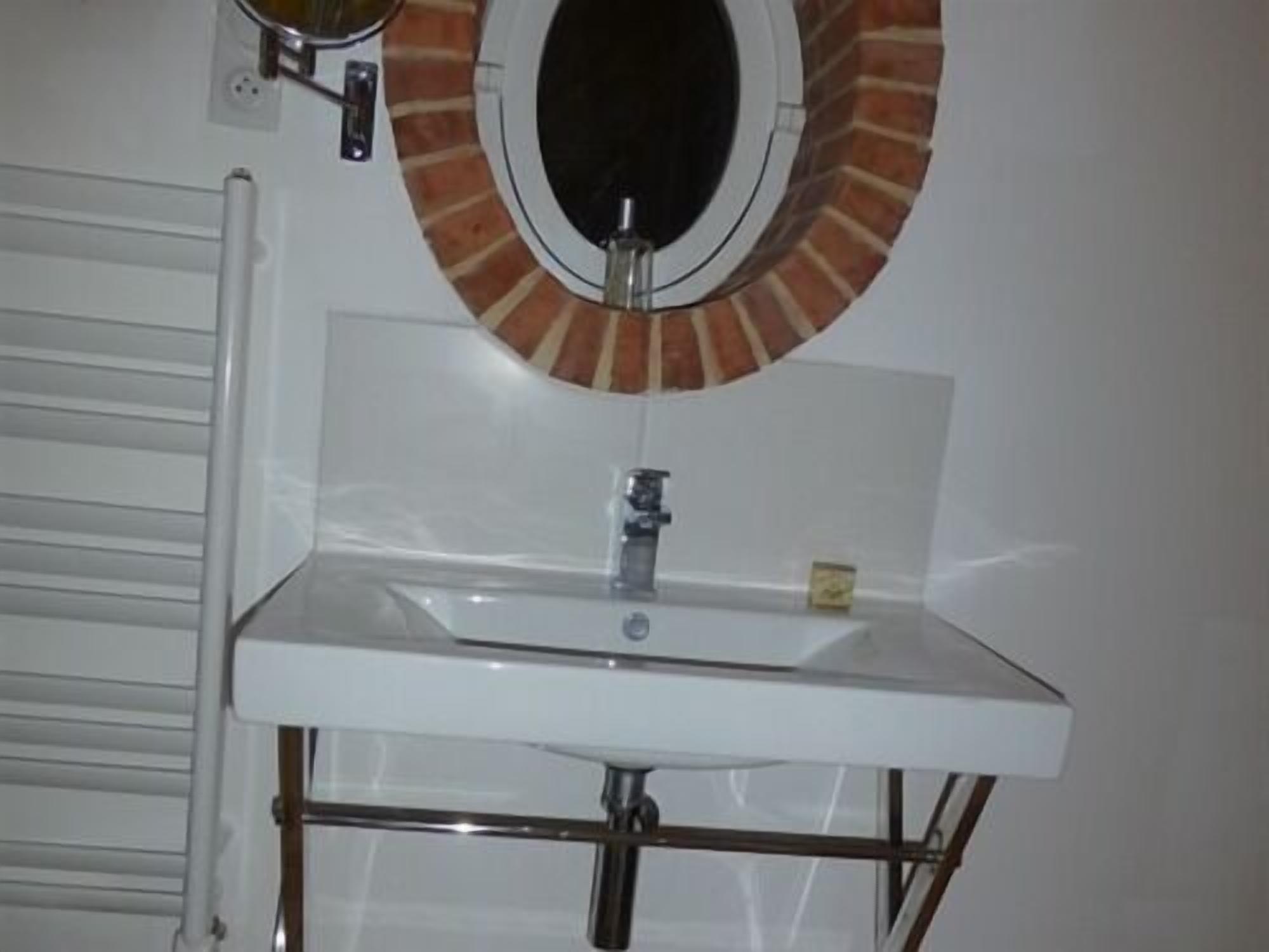 Une salle de bain avec un lavabo blanc, un miroir rond orné d’une bordure évoquant des briques, et un porte-serviettes blanc.