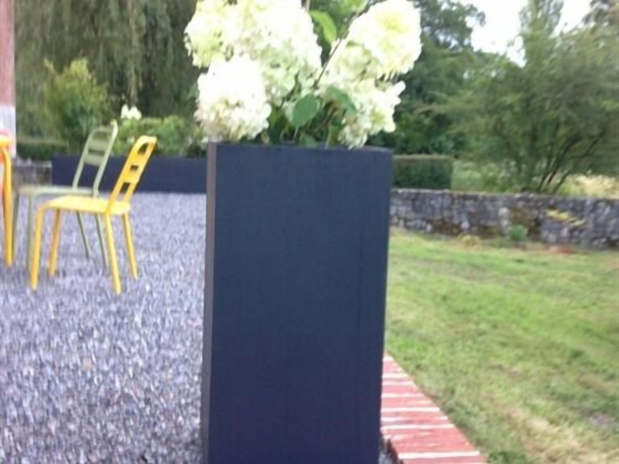 A garden area with a black planter box containing white flowers, a yellow chair, and a paved walkway.