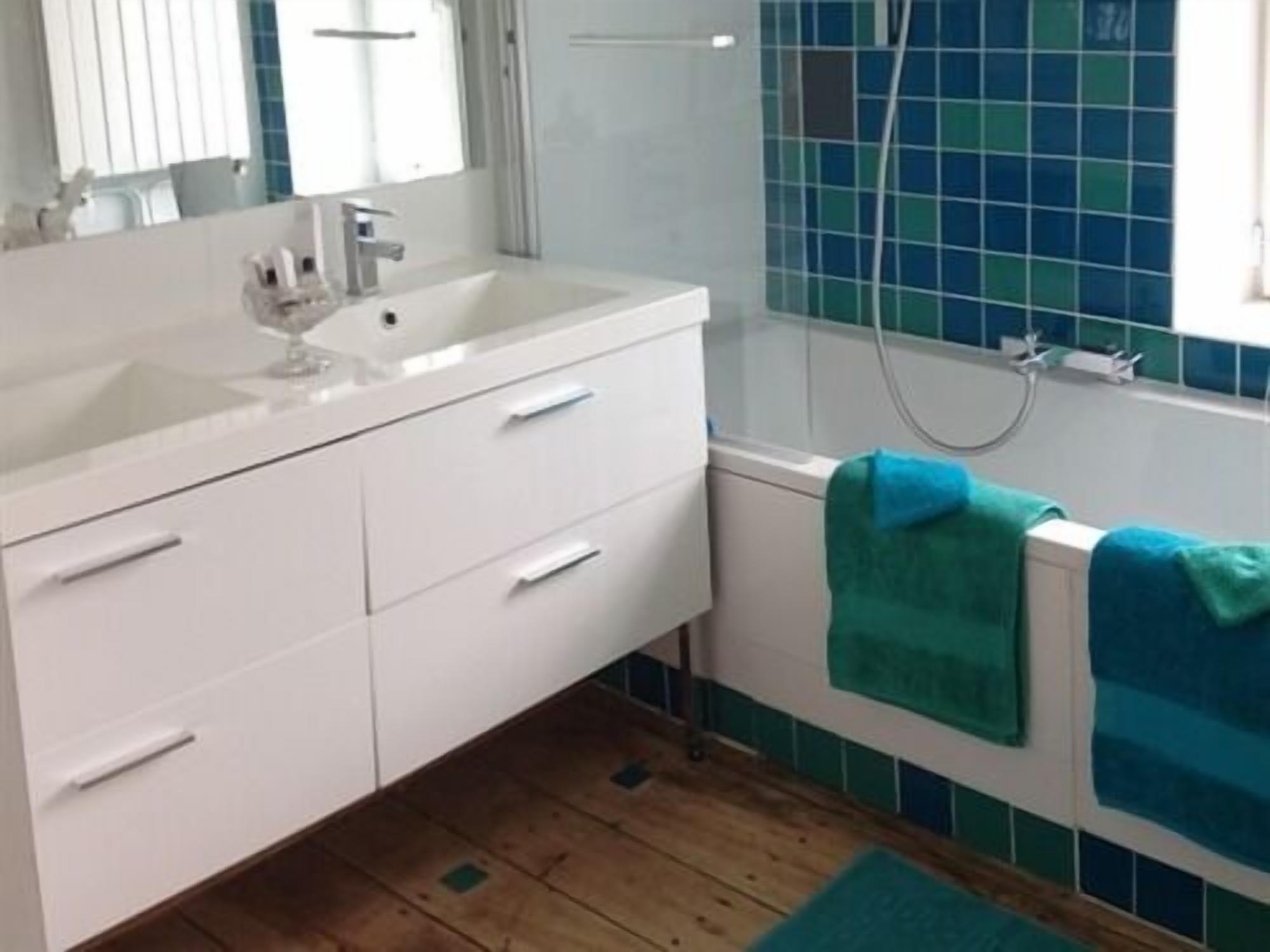 Een badkamer met een wit wastafelmeubel, een badkuip en blauwe betegelde wanden.