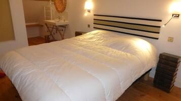 Ein Schlafzimmer mit einem großen Bett, Holzboden, weißem Kopfteil, einem Nachttisch, einer Lampe und einer kleinen Mülleimer.