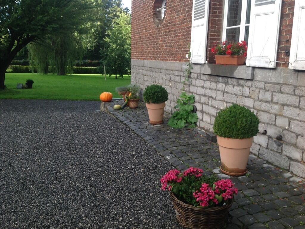 A brick building with a gravel driveway, potted plants, and a tree in the background.