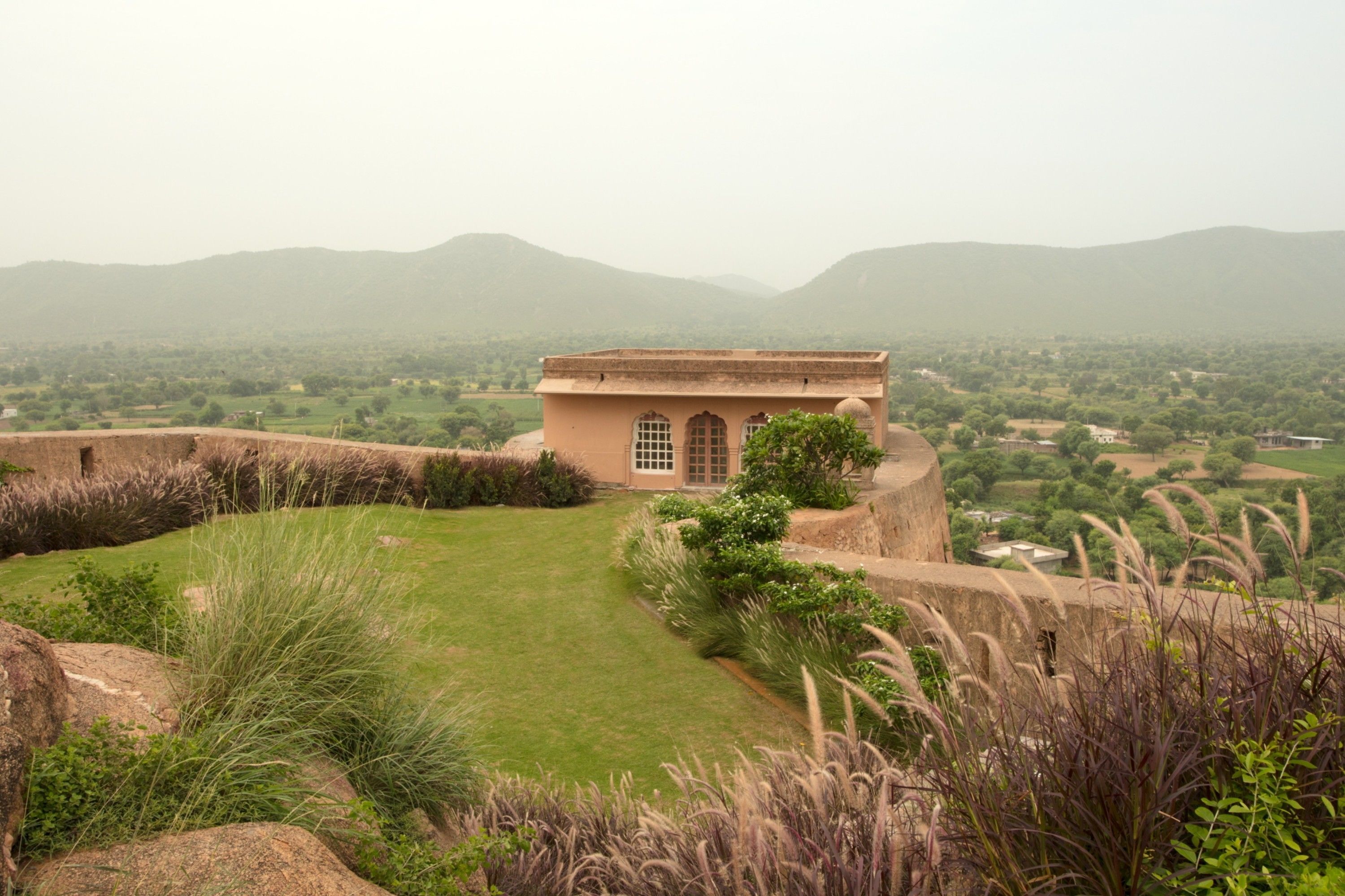 A historic building with a central courtyard, surrounded by lush greenery and distant hills.