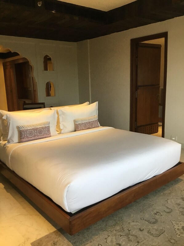 Una cama grande con ropa blanca y almohadas estampadas, un cabecero de madera y una puerta a la derecha.