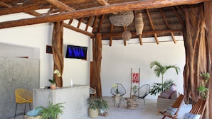 Un espacio de estar al aire libre cubierto con muebles de madera, plantas en macetas y una pantalla de televisión.