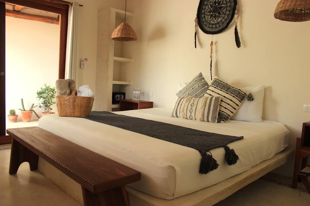 Een slaapkamer met een groot bed, een bankje, een mand en een wandplank.