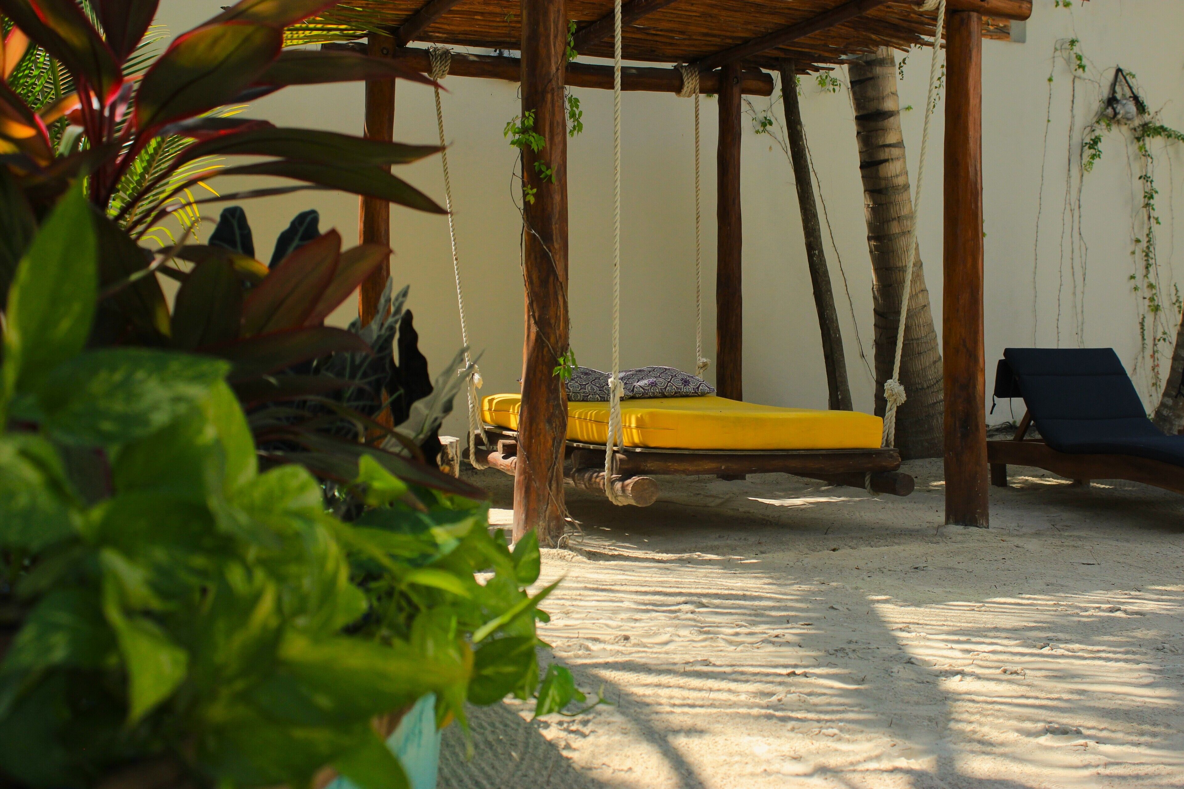 A beachside cabana with a hammock, a yellow bed, and lounge chairs.