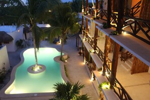 Un área de piscina con borde curvo, rodeada de palmeras y una terraza de madera con barandillas.