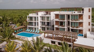 Un hotel de varios pisos con piscina, balcones y vistas al entorno verde.