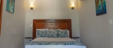 A neatly made bed with a wooden headboard, two wall-mounted lights, and two paintings on the walls.