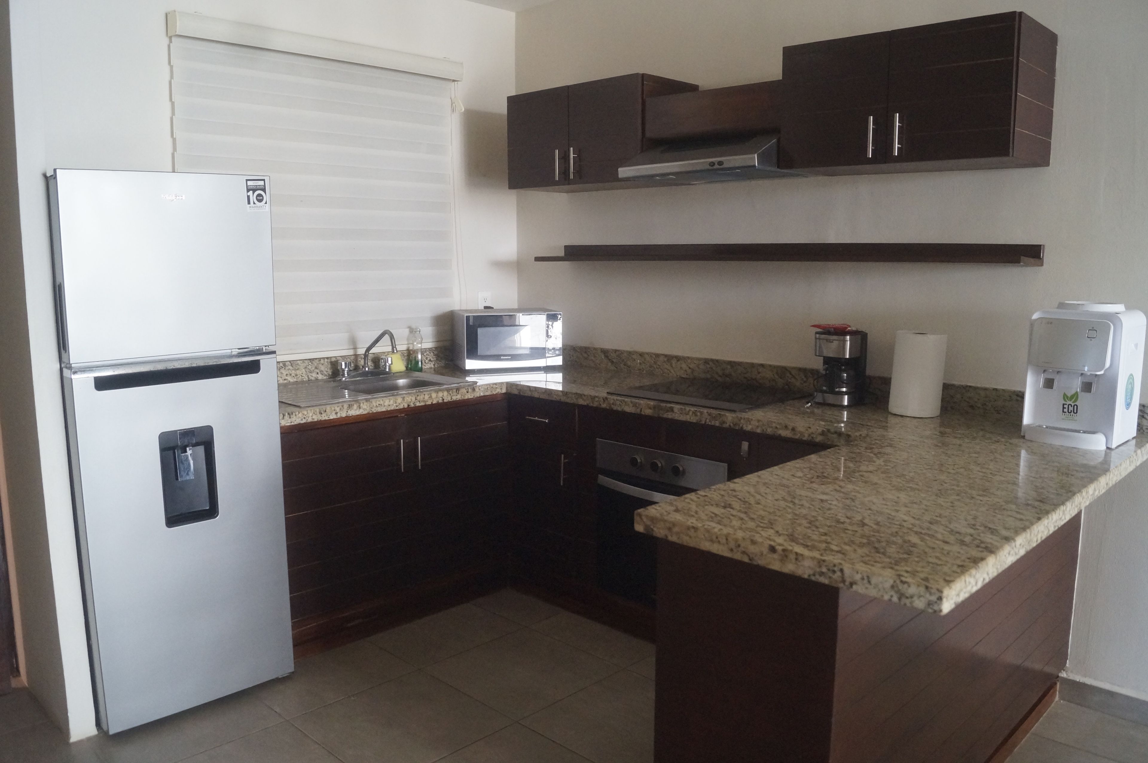 Una cocina compacta equipada con refrigerador, microondas, cafetera y horno integrado.