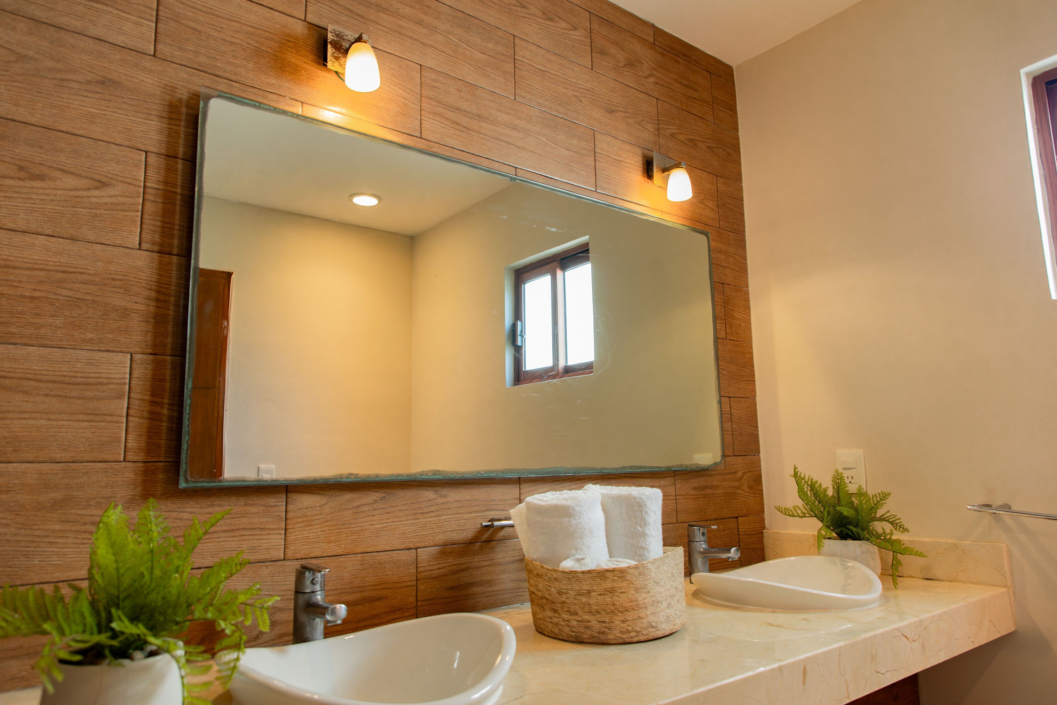 A bathroom with wooden paneling, a large mirror, two sinks, and a window.