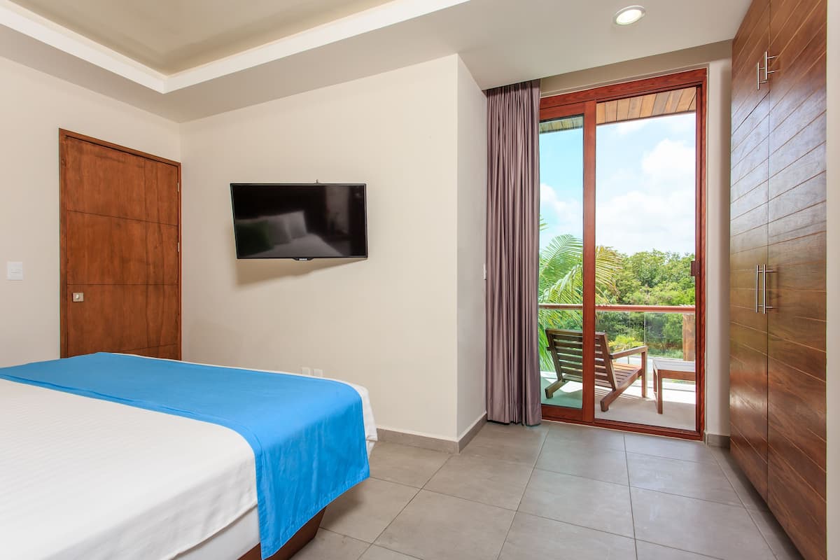 Een hotelkamer met een bed, een televisie, een glazen schuifdeur naar een balkon en houten kasten.