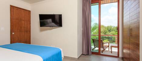 A hotel room with a bed, a TV, a sliding glass door to a balcony, and wooden cabinets.