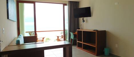 Habitación con una ventana grande, un televisor en la pared, un escritorio de madera y un pequeño rincón de estar con sillas.