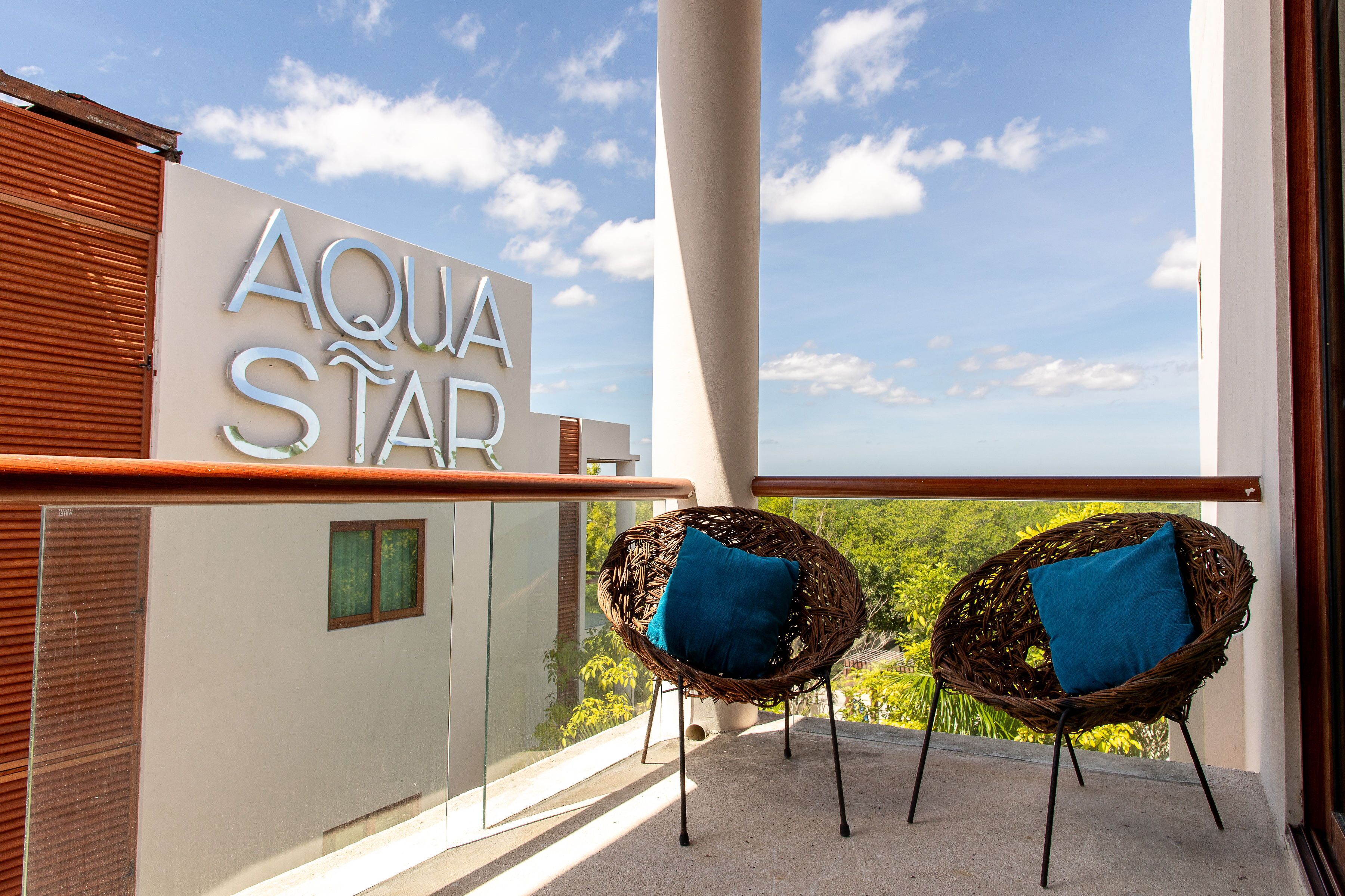 Un balcón con dos sillas de mimbre, un letrero que dice "AQUA STAR" y vista a zonas verdes.