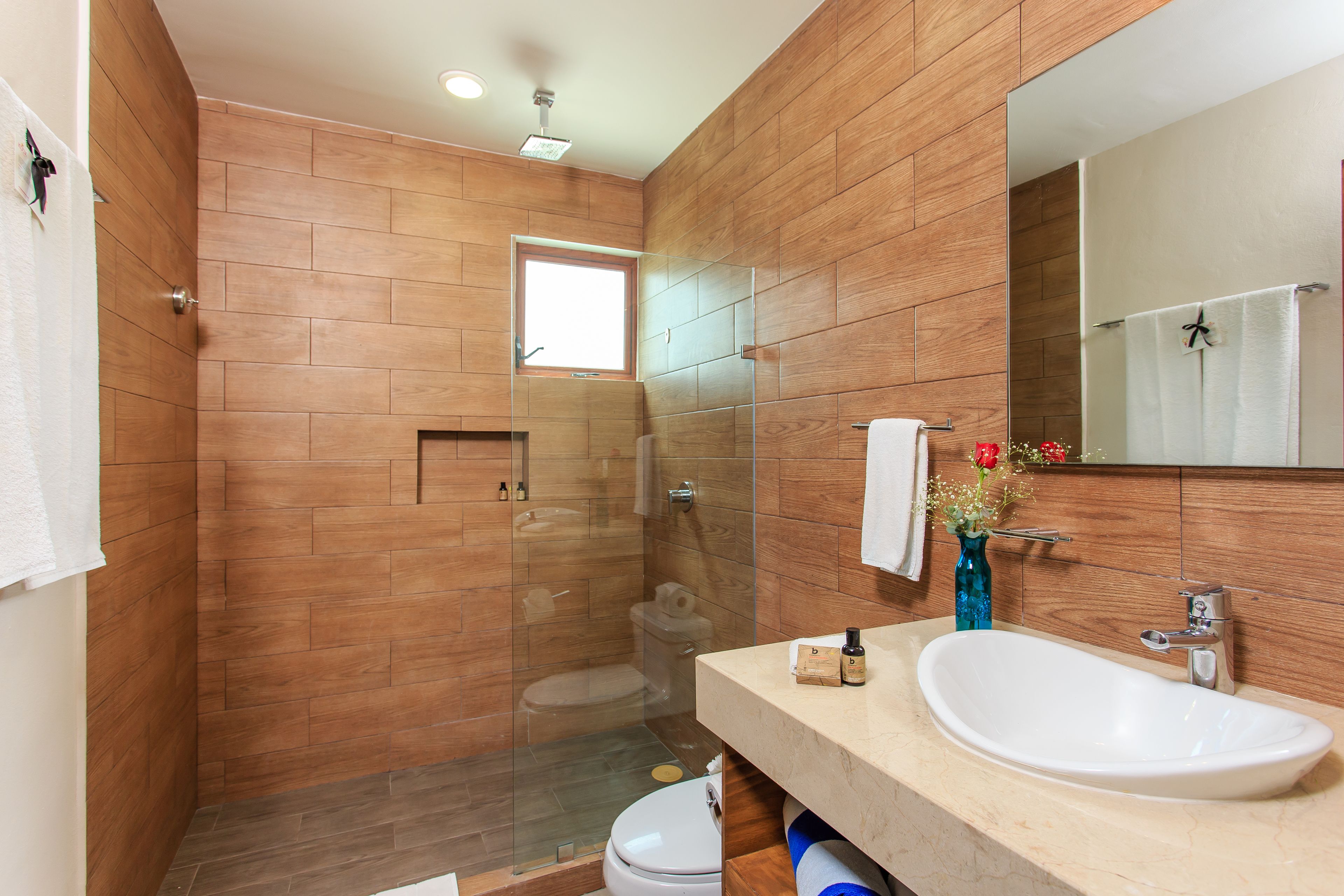 A modern bathroom with a wooden wall design, a glass-enclosed shower, a white sink, and a large mirror.