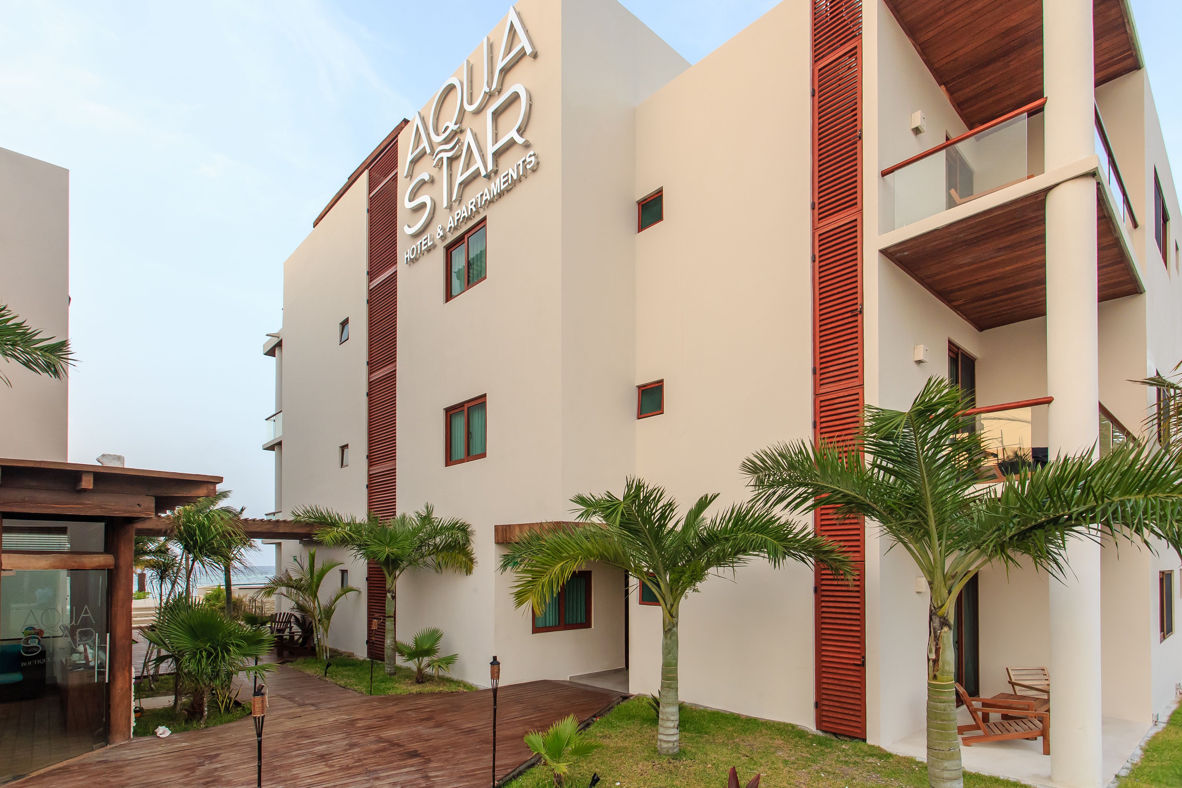 Un hotel moderno llamado "Aqua Star" con un diseño limpio, que cuenta con balcones y un área exterior bien cuidada con palmeras.