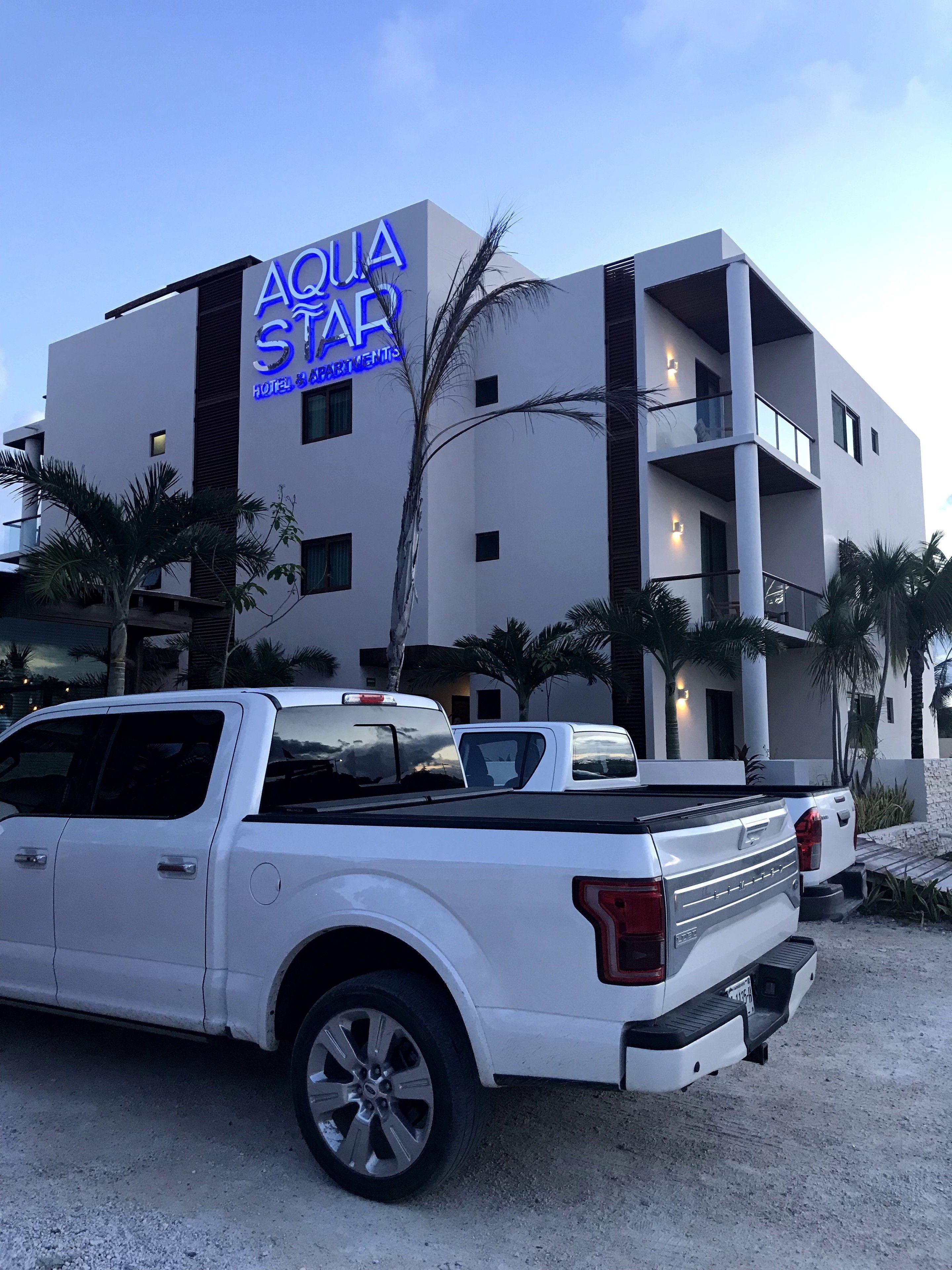 A white pickup truck parked in front of a building with a sign reading "AQUA STAR HOTEL & APARTMENTS".