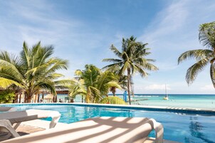 Un área de piscina con sillones de descanso, palmeras y vista al océano.