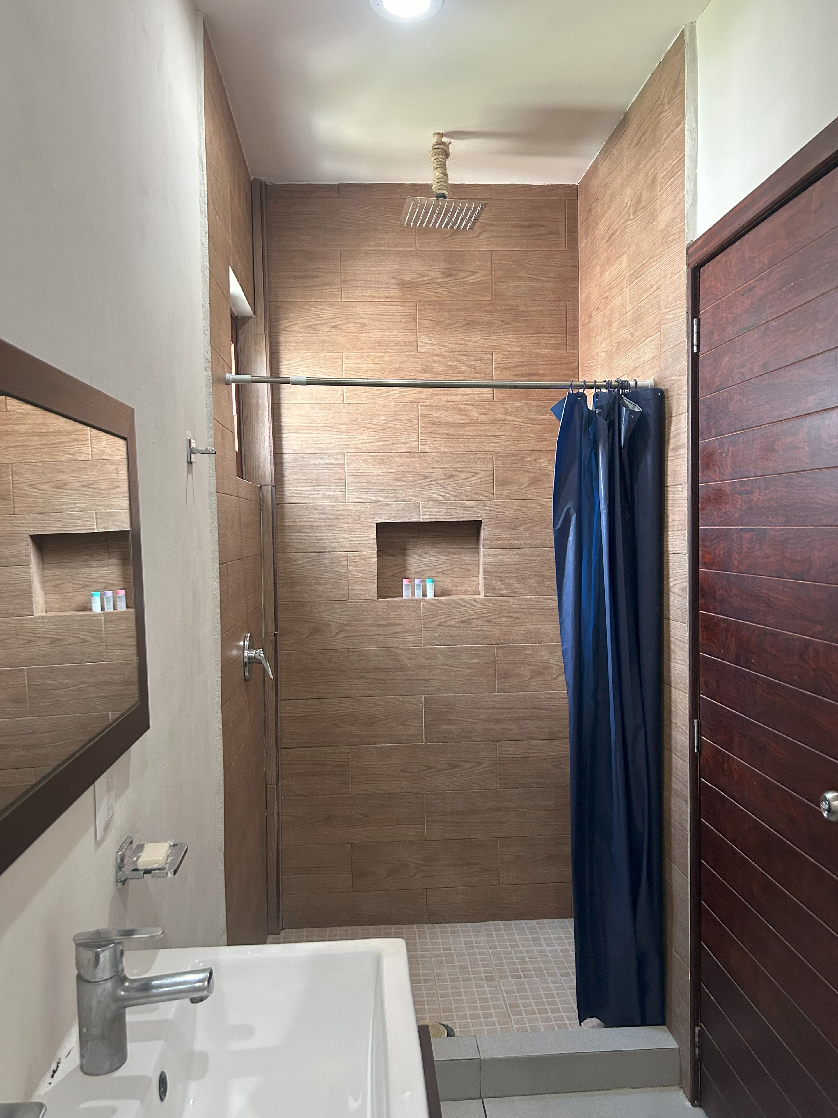 A modern bathroom with a wooden wall, a shower curtain, a bathtub, and a mirror.