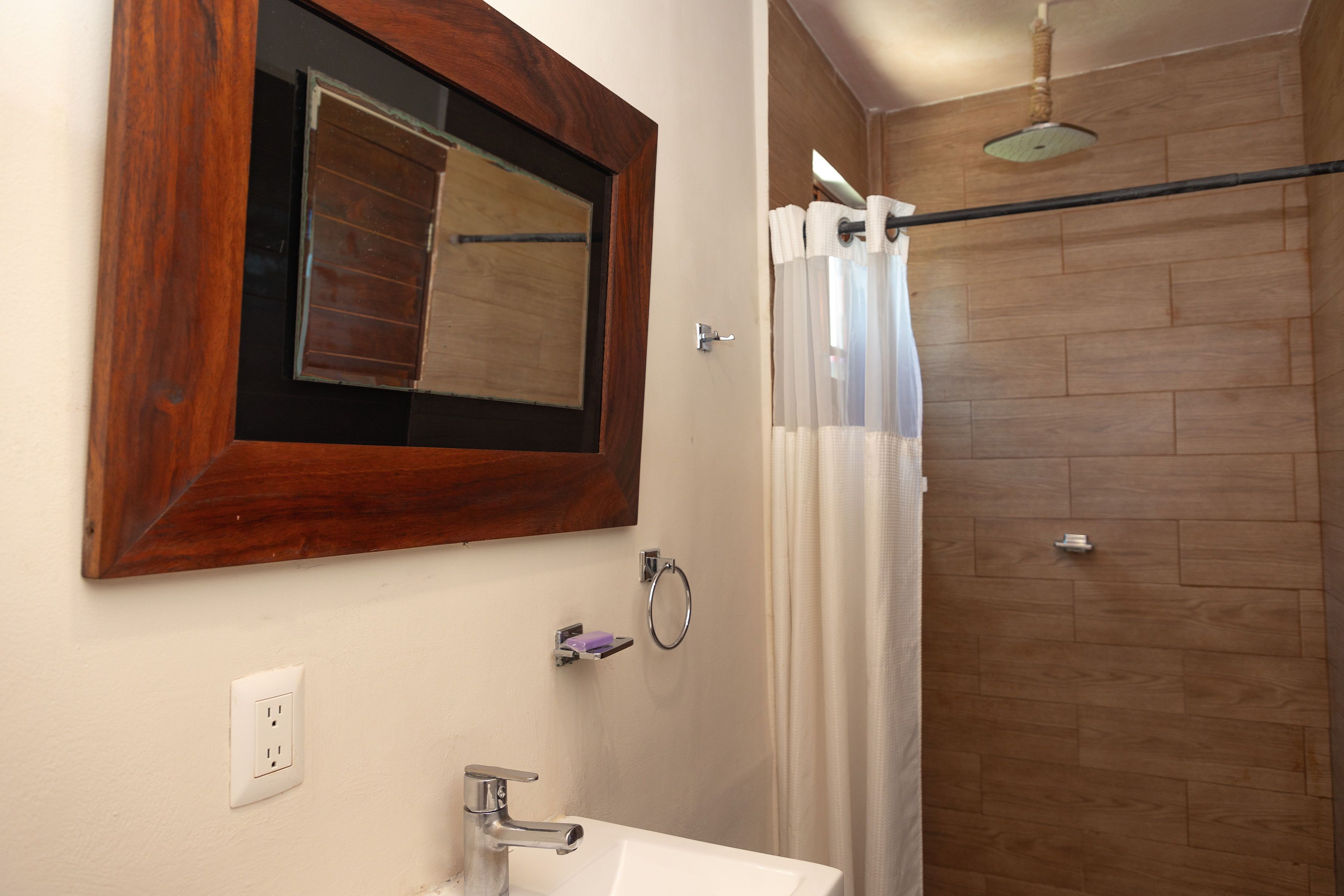 A bathroom with a wooden floor, a white sink, a mirror with a wooden frame, and a shower curtain.
