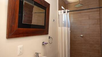A bathroom with a wooden floor, a white sink, a mirror with a wooden frame, and a shower curtain.