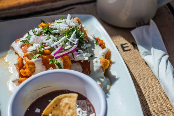A plate of nachos topped with cheese, onions, and cilantro, accompanied by a small bowl of salsa. - Aquastar Hotel & Apartments (Mahahual)