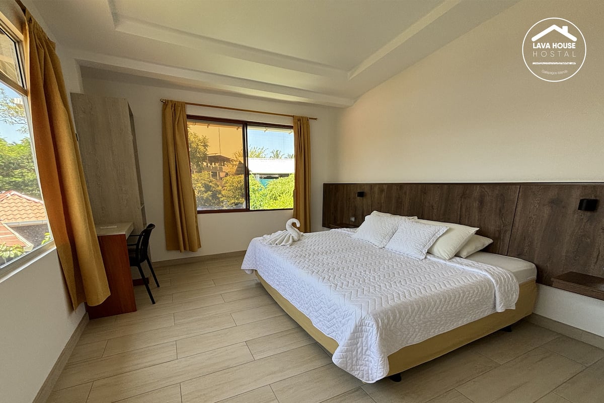Un dormitorio con cama, escritorio y ventana con cortinas.