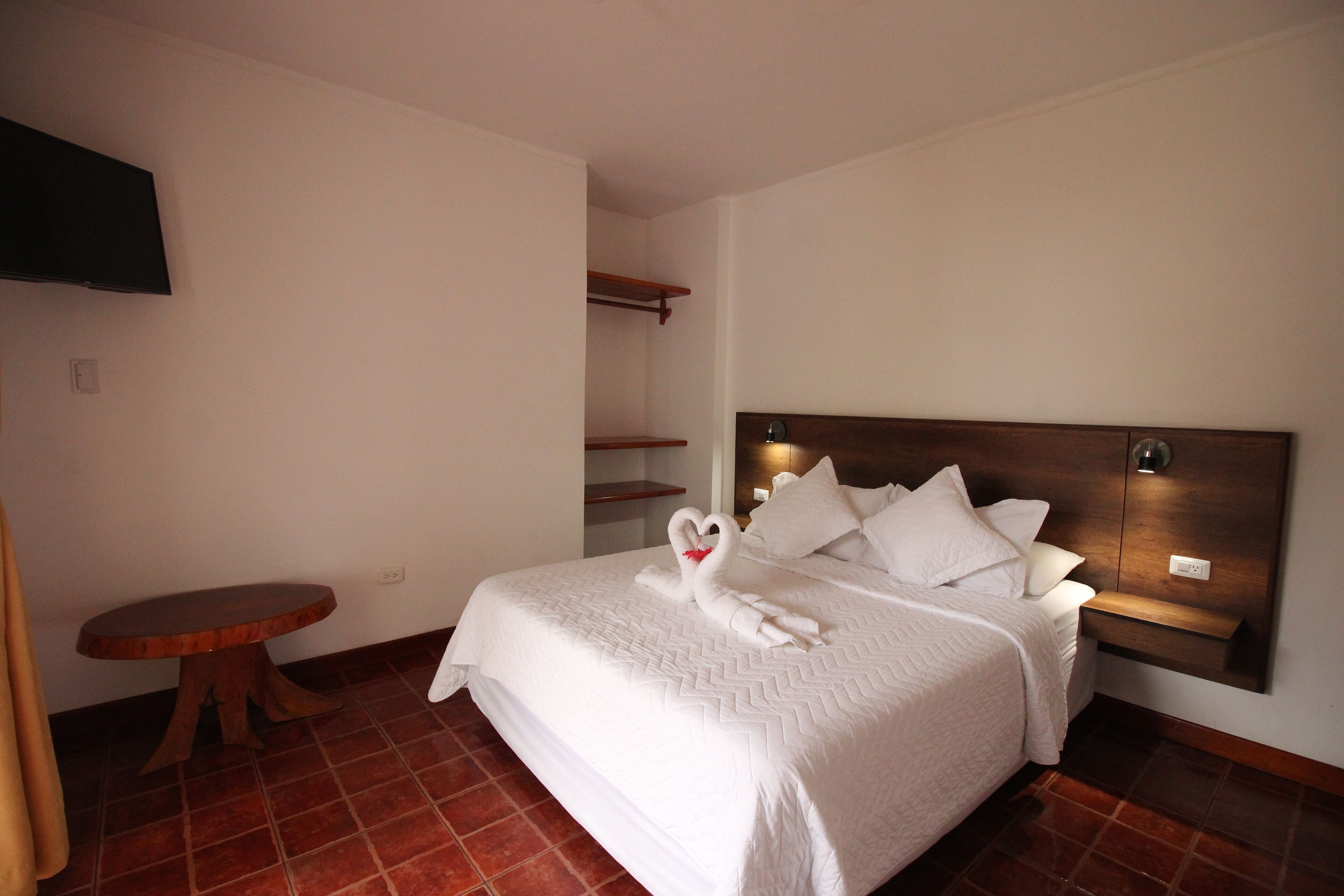 A neatly made bed with white bedding and pillows, a wooden headboard, and a small wooden table beside the bed.