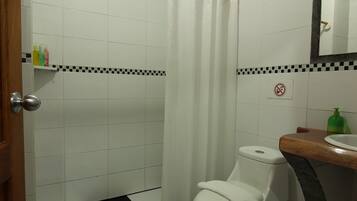 Een badkamer met een zwart-wit geruite vloer, een wit toilet, een douchegordijn en een houten wastafelmeubel met spiegel.