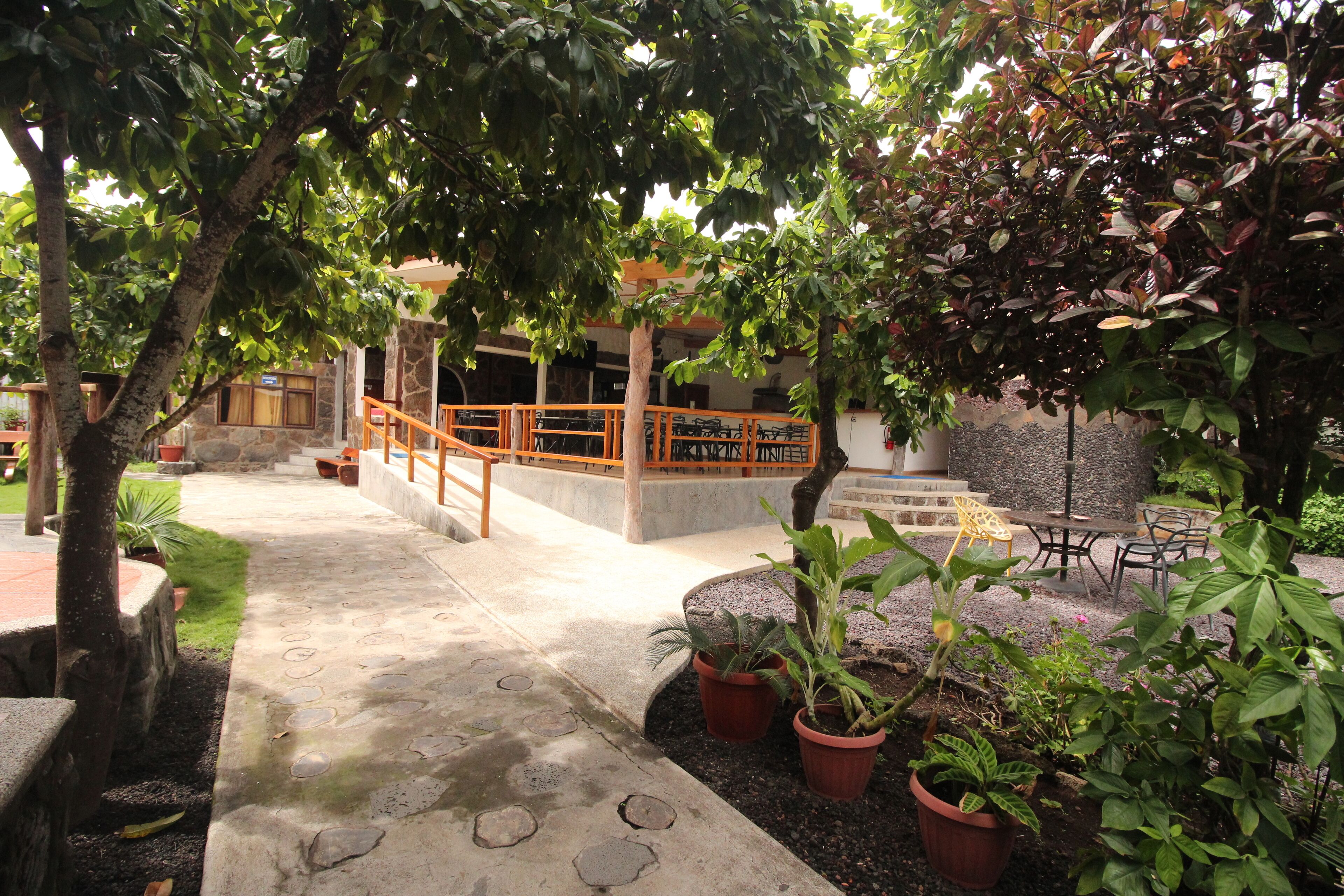 A courtyard with a stone pathway, potted plants, outdoor seating, and a staircase leading to an upper level.
