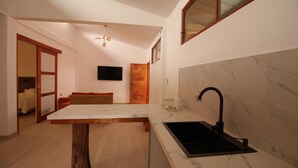 Eine moderne Küche mit Marmorarbeitsplatte, einem Holzesstisch, einem schwarzen Spülbecken und einem an der Wand befestigten Fernseher.