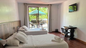 Ein Hotelzimmer mit zwei Betten, einem Schreibtisch, einem Sessel und einem Fernseher, mit Blick ins Freie.