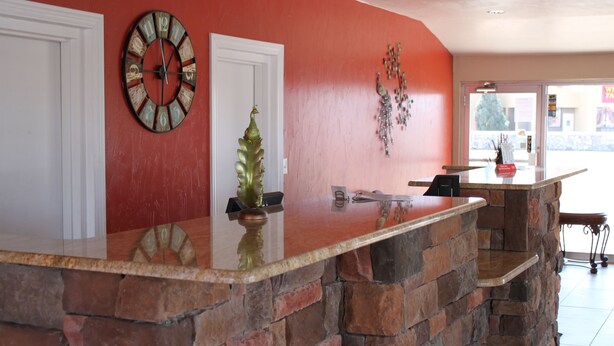 A reception area with a stone counter, a clock, and a decorative plant. - Century 21 Motel (Las Cruces)
