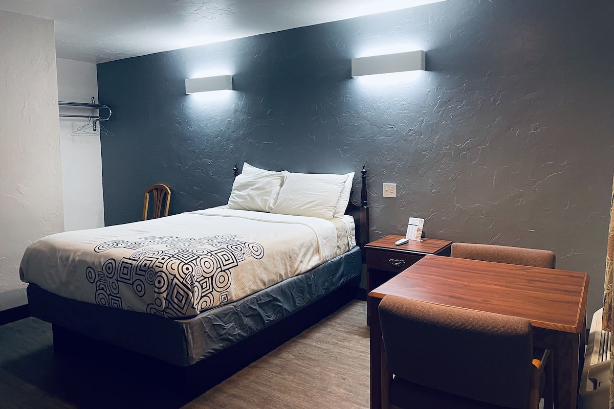 A hotel room with a bed, bedside table, and a small wooden table.