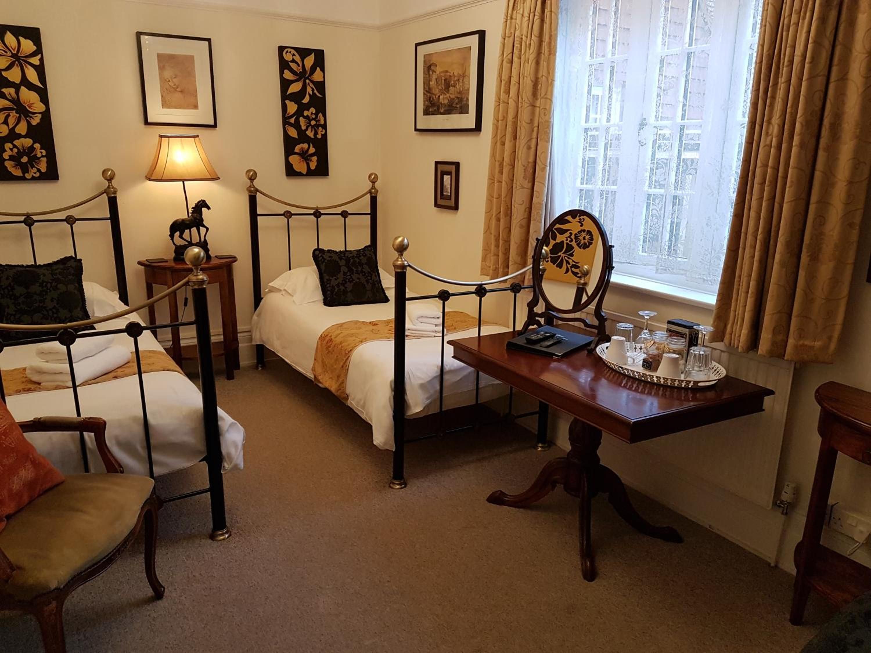 A hotel room with two beds, a wooden table with a tray of breakfast items, and a window with curtains.