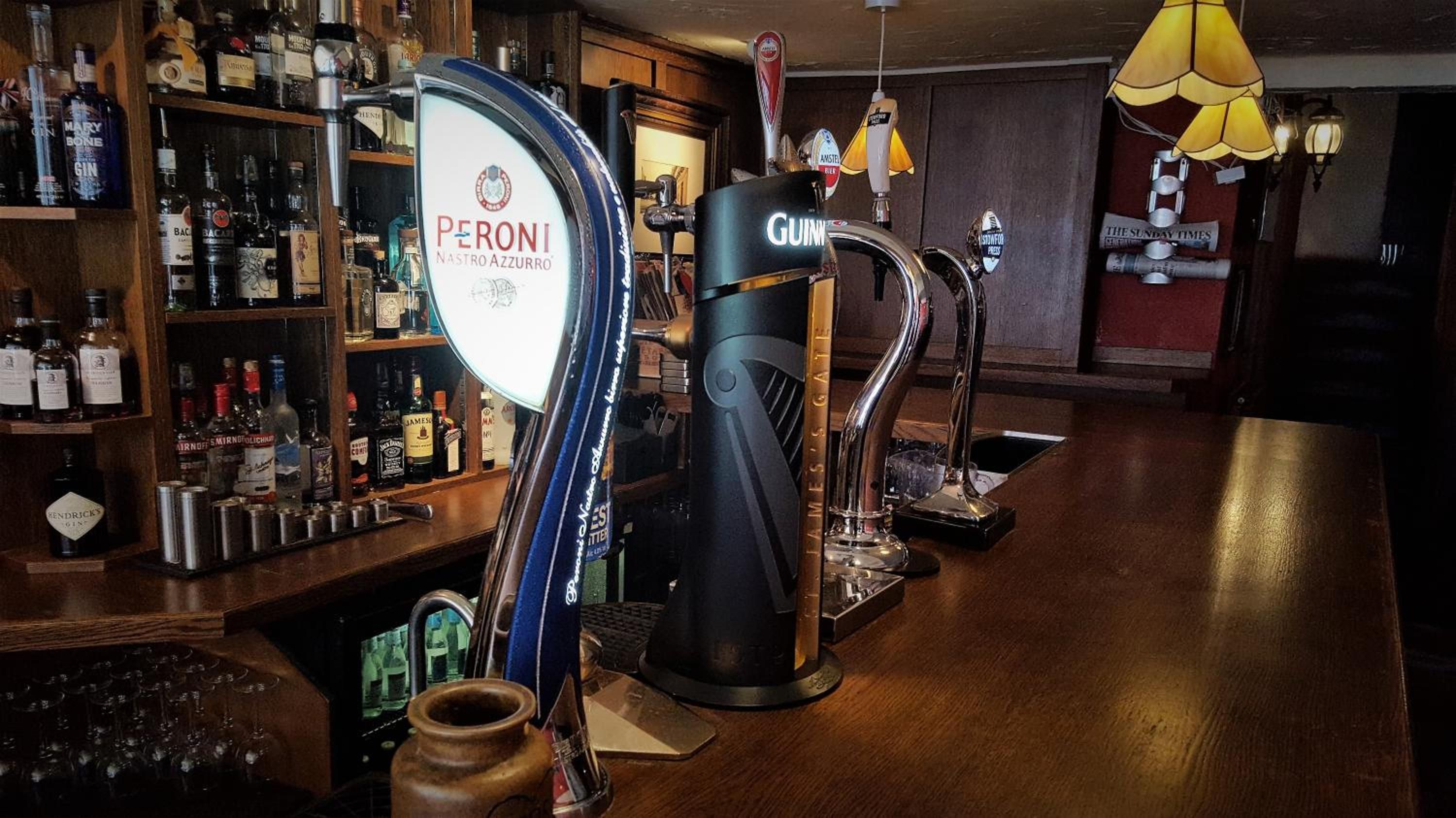 A bar with multiple taps, including Peroni and Guinness, and a variety of bottles and glasses on shelves.