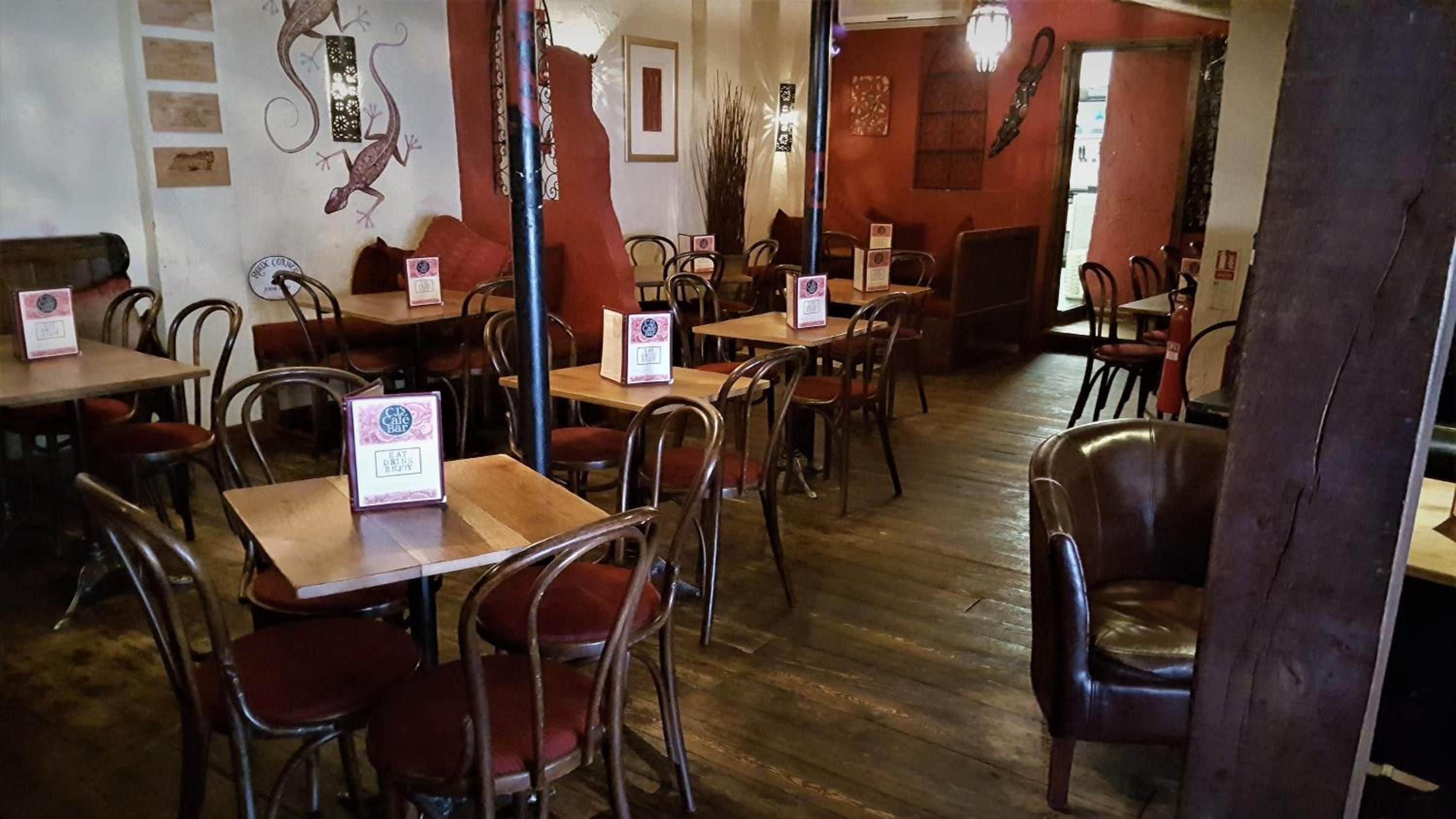 Een restaurantinterieur met houten tafels en stoelen, een menukaartstandaard en wanddecoraties.