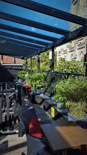An outdoor seating area with tables and chairs, surrounded by greenery and a view of a historic building.