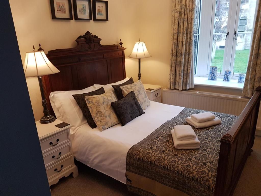 A neatly made bed with a patterned bedspread, two bedside lamps, a nightstand with drawers, and a window with curtains.